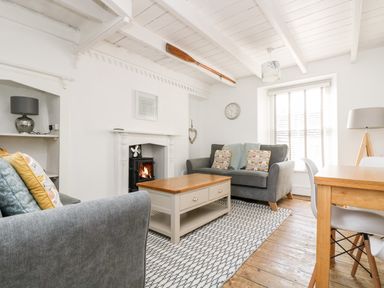 A living room with two grey sofas a wooden coffee table a fireplace and a dining table at Mole Cottage in Mousehole