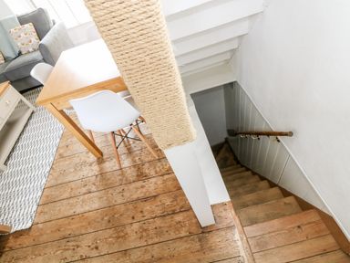 A wooden dining table with white chairs next to a staircase with wooden steps in a room with wooden floors at Mole Cottage in Mousehole