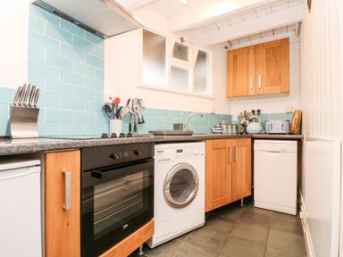 A kitchen with wooden cabinets blue tiled backsplash and appliances at Mole Cottage in Mousehole