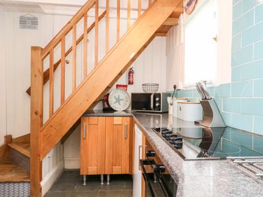 A kitchen with wooden stairs a microwave a knife set and blue tiled walls at Mole Cottage in Mousehole