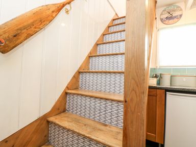 A wooden staircase with patterned risers and a wooden paddle on the wall next to a kitchen area at Mole Cottage in Mousehole