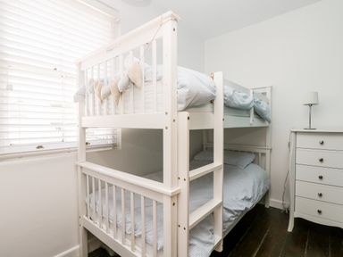 A bedroom with a white bunk bed and a white chest of drawers with a lamp at Mole Cottage in Mousehole