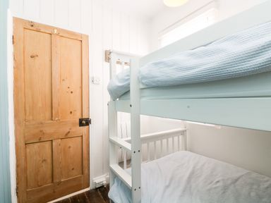 A small bedroom with a wooden door and white bunk beds with blue and white bedding at Mole Cottage in Mousehole
