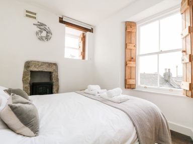 A bedroom with a made bed with pillows and rolled towels by a window with wooden shutters at Mole Cottage in Mousehole