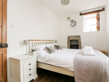 A bedroom with a bed nightstands lamps a window and a stone fireplace at Mole Cottage in Mousehole