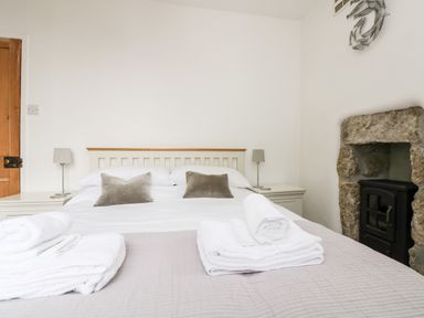 A bedroom with a double bed two bedside tables with lamps folded towels on the bed and a stone fireplace at Mole Cottage in Mousehole