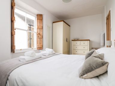A bedroom with a bed with pillows and towels near a window with wooden shutters a wardrobe and a chest of drawers at Mole Cottage in Mousehole