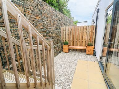 An outdoor area with wooden stairs a pebble ground a wooden bench with plants on each side and a stone wall at Seaspell Beach House in Constantine Bay