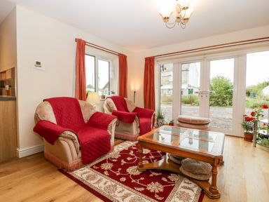 A living room with two armchairs and a coffee table on a patterned rug with glass doors leading outside at Vine Lodge in Kingsbury Episcopi near Martock