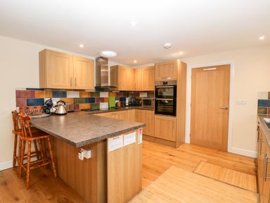 A kitchen with wooden cabinets a countertop with two stools and colorful tiled backsplash at Vine Lodge Kingsbury Episcopi near Martock