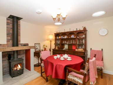 A dining room with a red tablecloth on a round table and a wood-burning stove at Vine Lodge in Kingsbury Episcopi near Martock