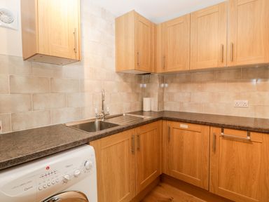 A kitchen corner with wooden cabinets a stainless steel sink a washing machine and tiled walls at Vine Lodge in Kingsbury Episcopi near Martock