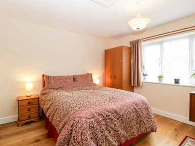 A bedroom with a bed covered in patterned bedding a wooden wardrobe bedside tables with lamps and a window with curtains and plants at Vine Lodge in Kingsbury Episcopi near Martock