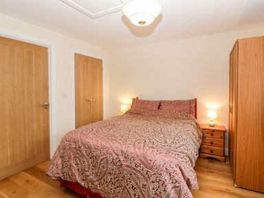A bedroom with a double bed with patterned bedding a wooden wardrobe two wooden doors and bedside tables with lamps at Vine Lodge in Kingsbury Episcopi near Martock