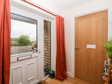 An entrance area with a white glass door and red curtains next to a wooden interior door with a note attached at Vine Lodge Kingsbury Episcopi near Martock