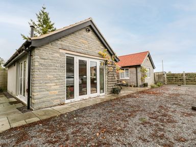 Two small stone and wood houses with red tile roofs and glass doors surrounded by gravel and pavement at Vine Lodge in Kingsbury Episcopi near Martock