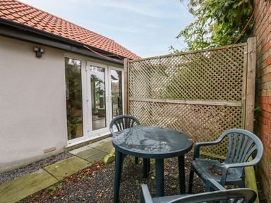 An outdoor patio area with a plastic table and chairs next to a house with glass doors and a lattice fence at Vine Lodge in Kingsbury Episcopi near Martock