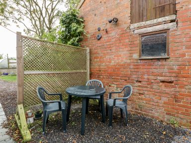 An outdoor seating area with three plastic chairs and a round table next to a brick wall and wooden lattice at Vine Lodge Kingsbury Episcopi near Martock