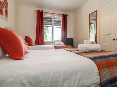 A bedroom with two single beds orange pillows red curtains and a mirror at Valley Lodge 48 in Callington