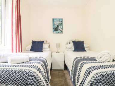 A bedroom with two single beds with blue patterned blankets and blue pillows separated by a white nightstand with a lamp at Valley Lodge 48 in Callington