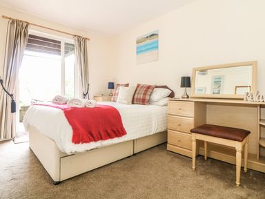 A bedroom with a bed with red throw blanket and rolled towels near a dressing table with mirror at Valley Lodge 48 in Callington
