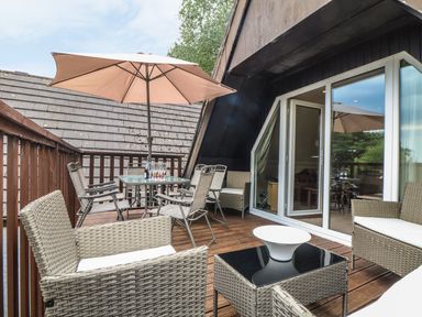 An outdoor wooden deck with wicker chairs a glass table with an umbrella and sliding glass doors at Valley Lodge 48 in Callington