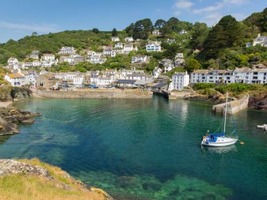 A coastal village with white houses on a hillside overlooking a harbor with a sailboat in water