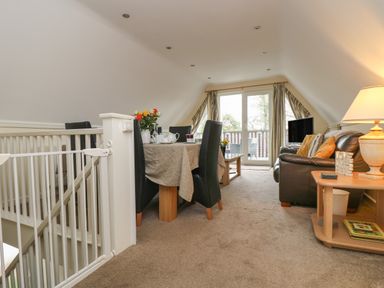 A living area with a dining table and black chairs a brown sofa a coffee table a side table with a lamp and the television at Valley Lodge 48 in Callington