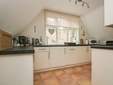 A kitchen with white cabinets black countertops a window with patterned blind and various appliances at Valley Lodge 48 Callington