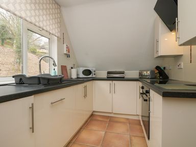 A kitchen with white cabinets black countertops a window with a patterned blind and small appliances at Valley Lodge 48 in Callington