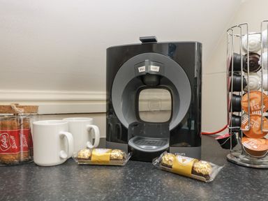 A coffee machine with two white mugs biscuits chocolates and a capsule holder at Valley Lodge 48 in Callington