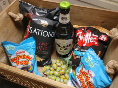 A wooden crate with two bags of Rainbow Drops candy packs two bags of crisps a bottle of Proper Job beer and a mesh bag of chocolate eggs in Valley Lodge 48 Callington