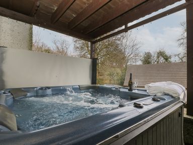 An outdoor covered hot tub with a bottle of champagne two glasses and a folded white robe at Valley Lodge 48 in Callington