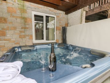 An outdoor hot tub with water flowing and a bottle with two glasses and a white towel at Valley Lodge 48 in Callington