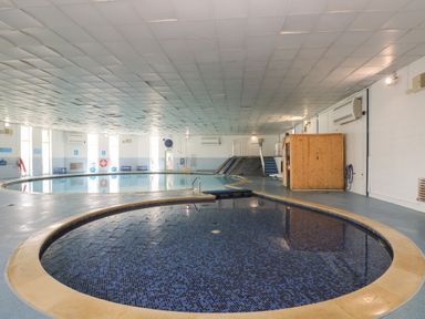 An indoor swimming pool area with a round shallow pool and a larger pool with a slide at Valley Lodge 48 in Callington