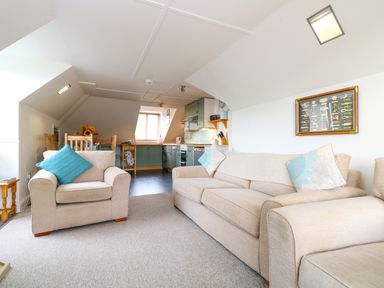 An open plan living room and kitchen with beige sofas and wooden dining table at The Watch in Porthcurno
