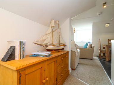A wooden cabinet with a model sailboat and books next to a seating area and dining table at The Watch in Porthcurno