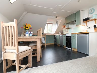 A kitchen and dining area with wooden chairs and table and green cabinets at The Watch in Porthcurno