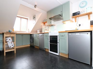 A kitchen with green cabinets a white oven a window and various appliances at The Watch in Porthcurno