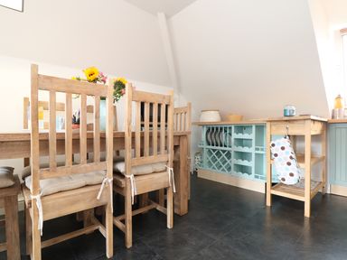 A dining area with wooden chairs and table and a kitchen counter with blue cabinets at The Watch in Porthcurno