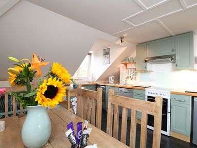 A kitchen with wooden table and chairs a vase with sunflowers and a stove at The Watch in Porthcurno