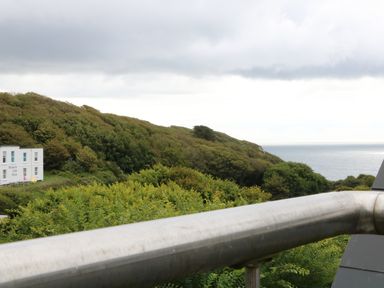 A view of green hills and the sea with a white building labeled museum cafe shop and a metal railing in the foreground at The Watch in Porthcurno