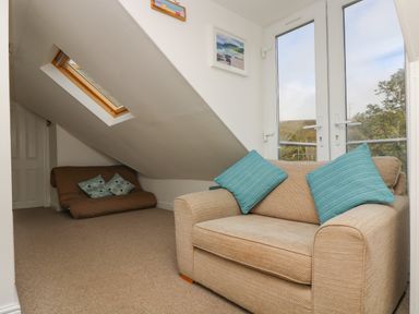 A room with two sofas and blue cushions under a sloped ceiling with a skylight and glass doors at The Watch in Porthcurno