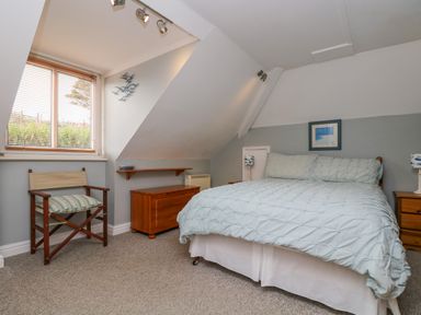 A bedroom with a bed wooden chest two wooden bedside tables and a chair by a window at The Watch in Porthcurno