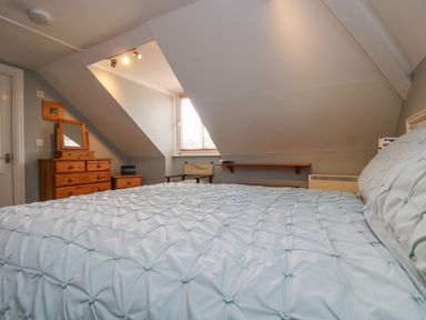 A bedroom with a bed covered in a light blue quilt a wooden dresser with a mirror a wooden chair and window at The Watch in Porthcurno