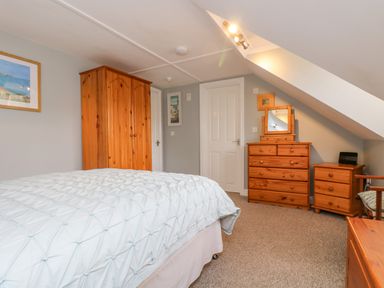 A bedroom with a bed, wooden wardrobe, chest of drawers with mirror, bedside table, and carpeted floor at The Watch in Porthcurno