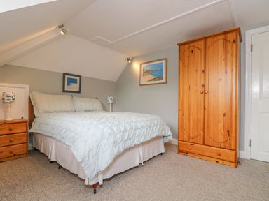 A bedroom with a bed a wooden wardrobe two lamps and framed pictures on the walls at The Watch in Porthcurno