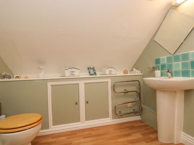 A bathroom with a toilet a pedestal sink green tiles and storage cabinets at The Watch in Porthcurno