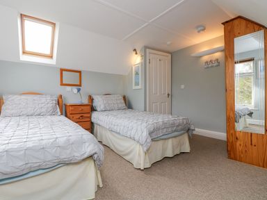 A bedroom with two single beds a wooden wardrobe with a mirror and a small nightstand at The Watch in Porthcurno