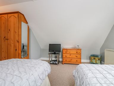 A bedroom with two beds a wooden wardrobe a small TV on a stand a wooden dresser and a decorative box at The Watch in Porthcurno